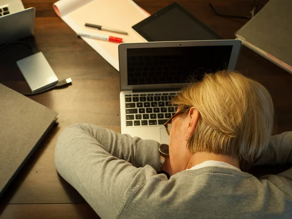 Totalement surmenée Une femme s'endort sur son ordinateur portable