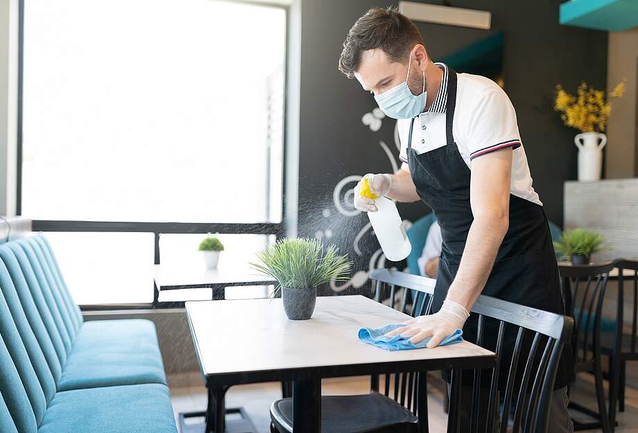 Un employé avec un masque nettoie une table dans une entreprise de restauration