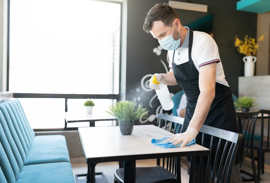 Un employé avec un masque nettoie une table dans une entreprise de restauration
