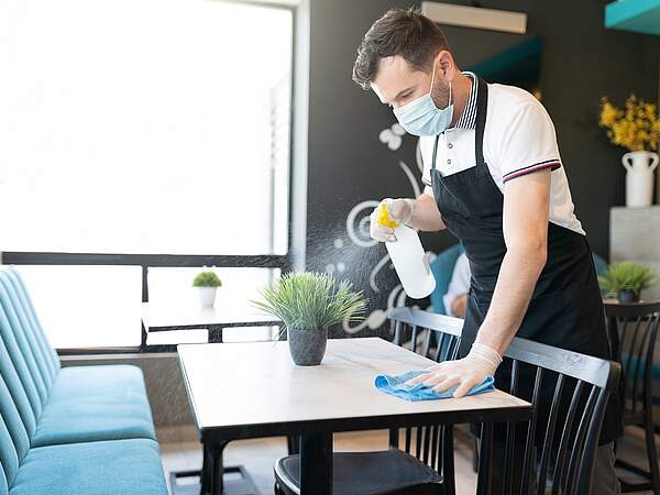 Un employé avec un masque nettoie une table dans une entreprise de restauration