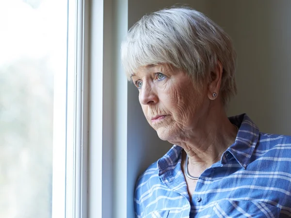 Une femme âgée qui regarde par la fenêtre avec un air triste