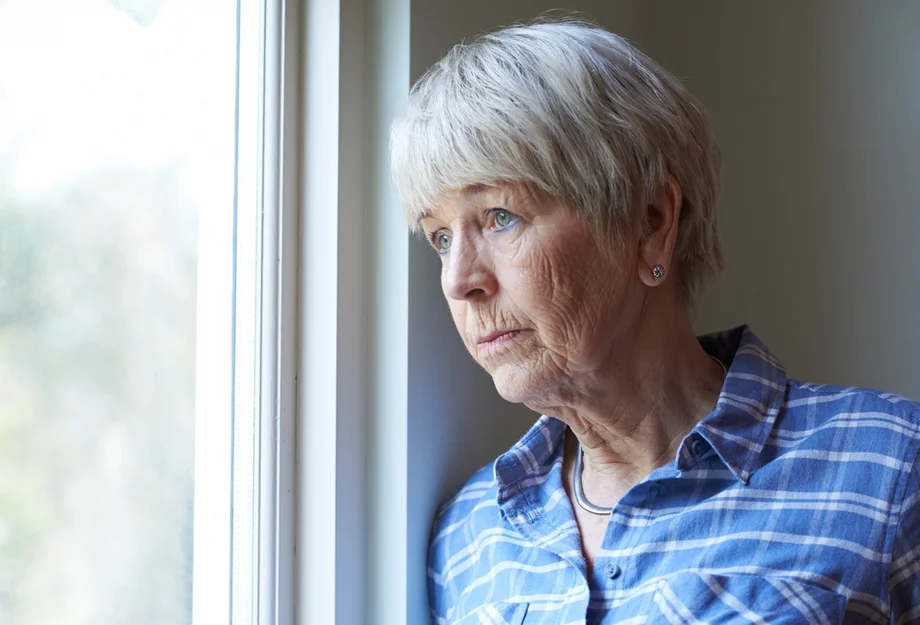 Une femme âgée qui regarde par la fenêtre avec un air triste